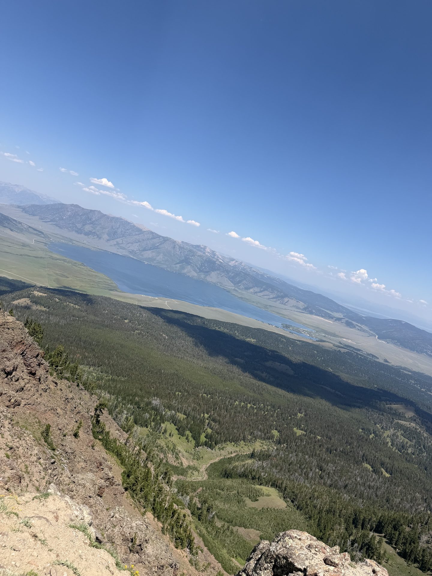 Hiking view from a rocky summit over a forested valley, a lake, and mountains
